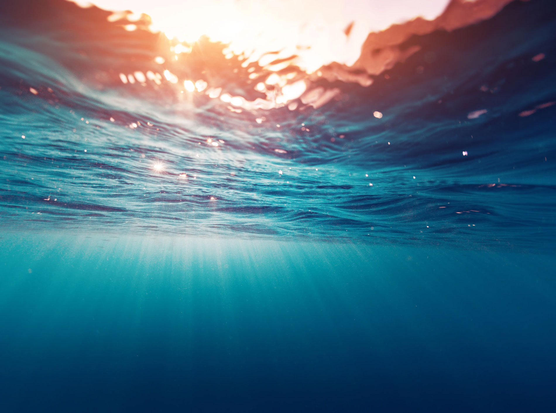 An underwater view of the ocean with open sun rays shining through the water.